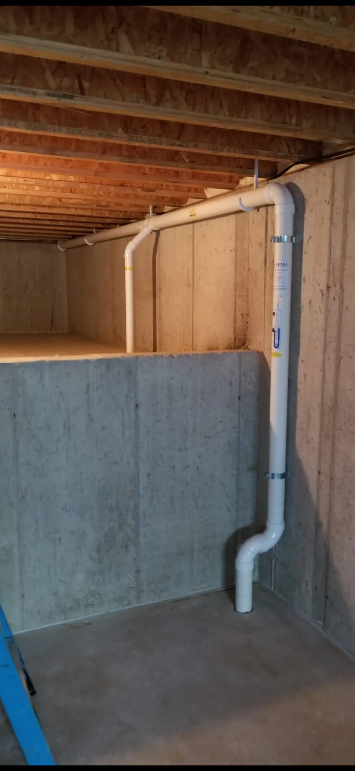 Clean PVC radon routing through joists and down to the slab in an unfinished basement.