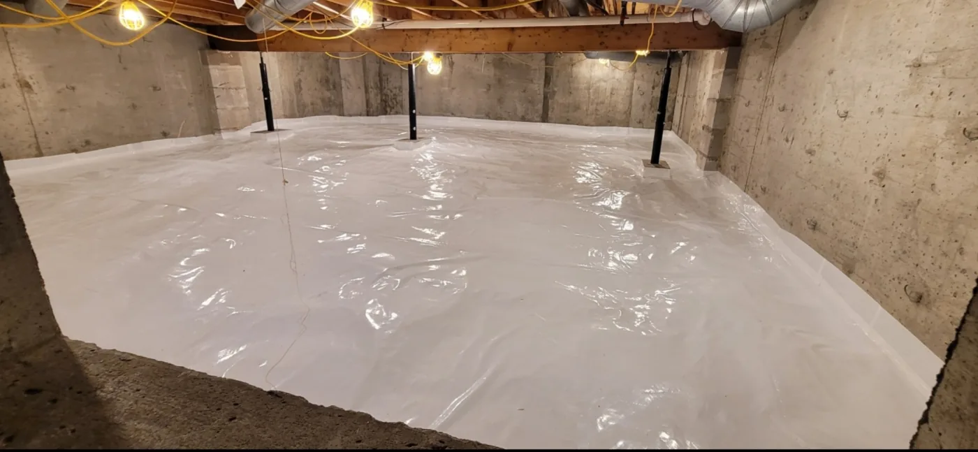 Crawl space fully encapsulated with a white vapor barrier covering the floor.