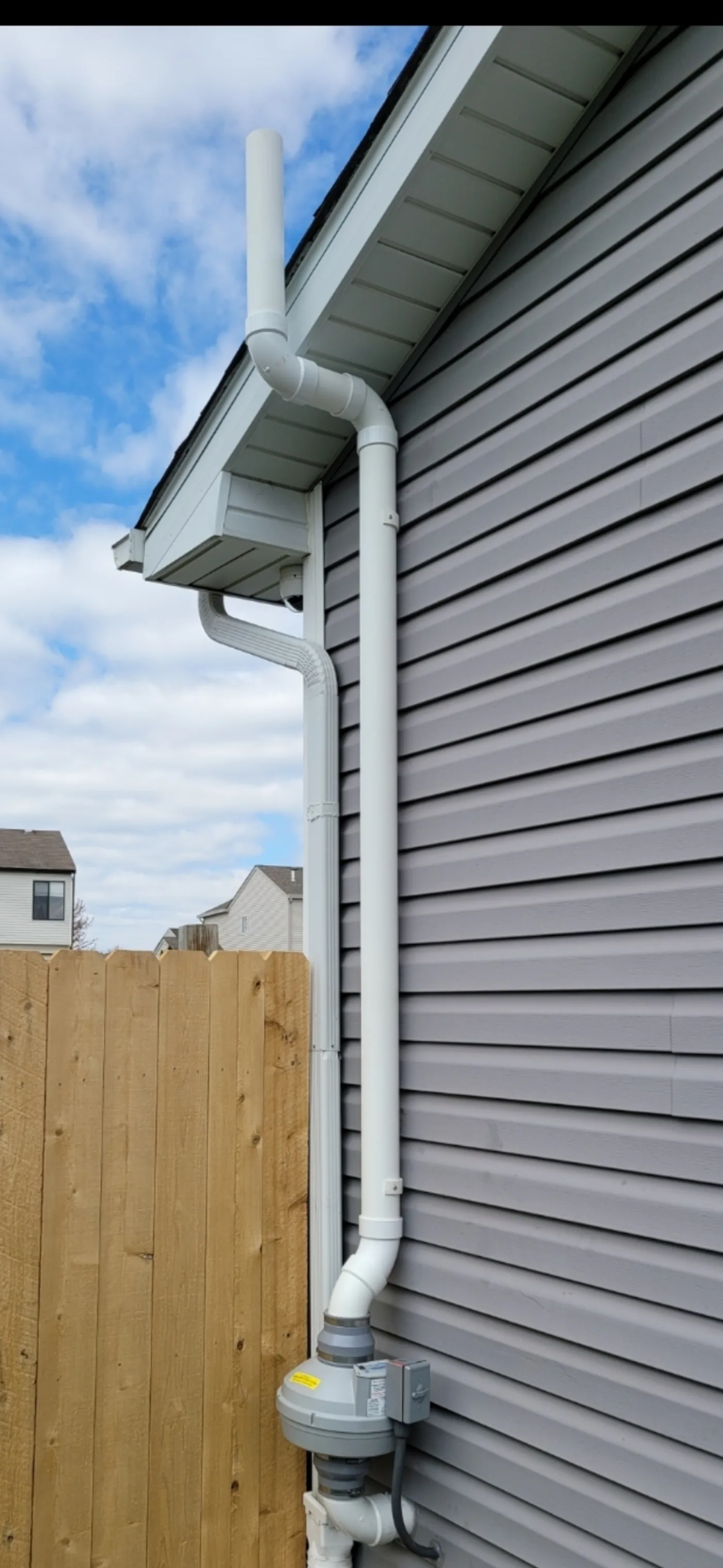 Gray vinyl-sided home with clean white PVC radon pipe running up the side past the eaves.