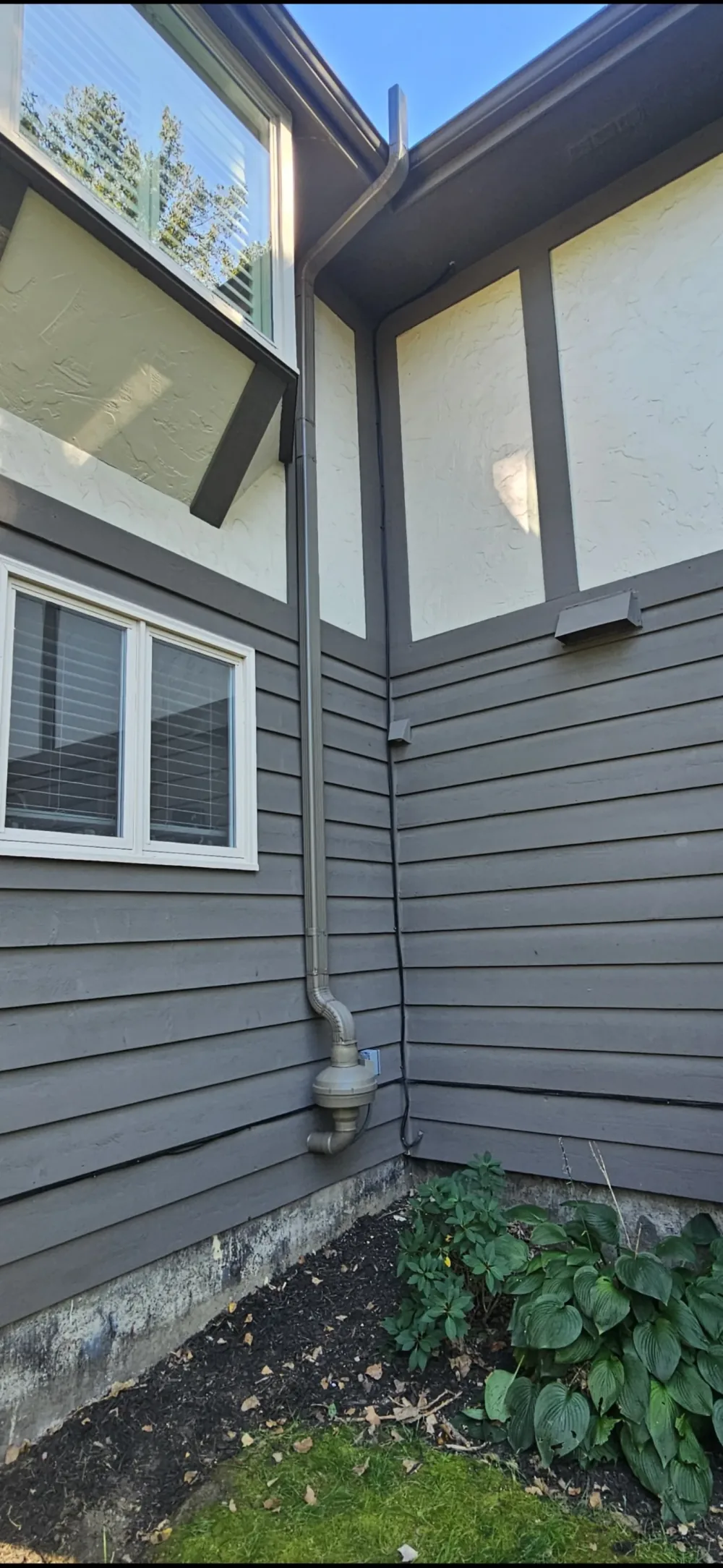 Tudor-style gray home with an aluminum radon downspout painted to match the house trim.