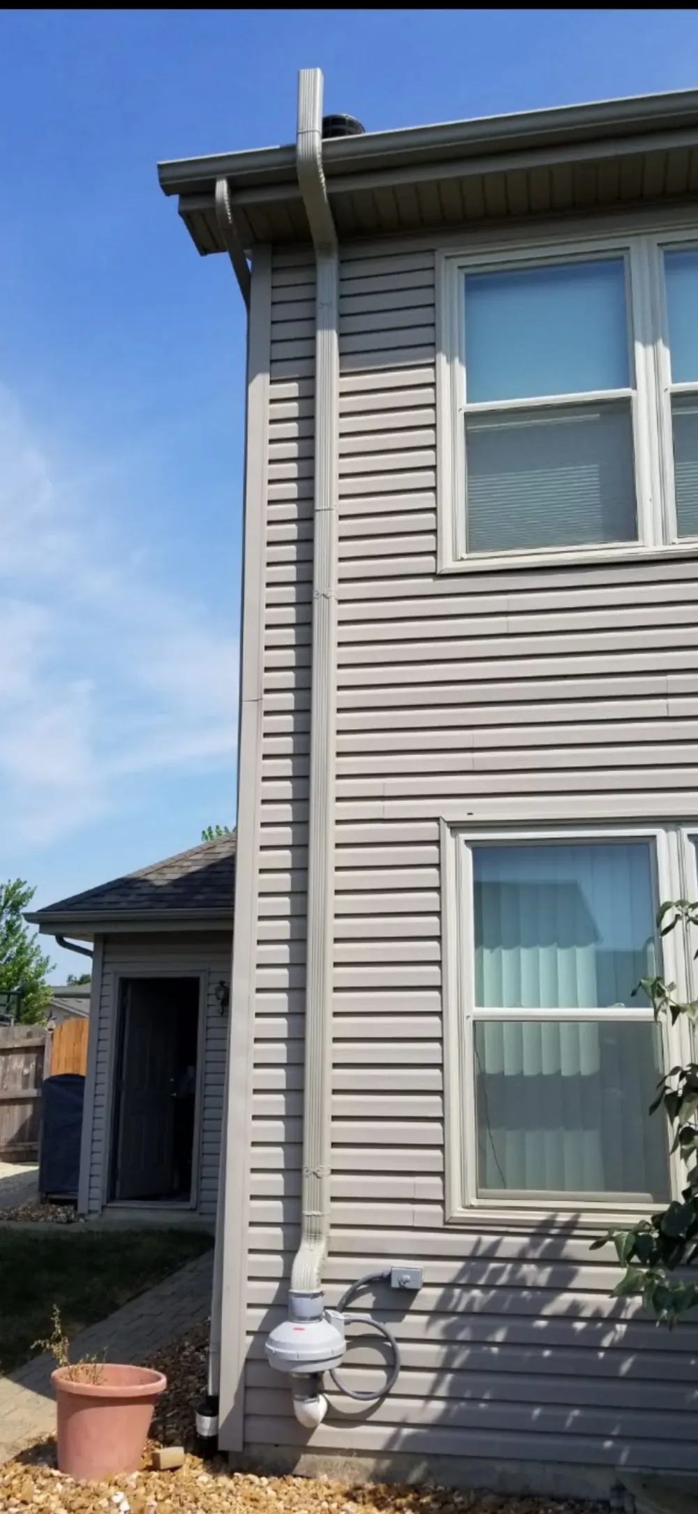Two-story suburban home with aluminum radon vent pipe running up the exterior siding to the roof.